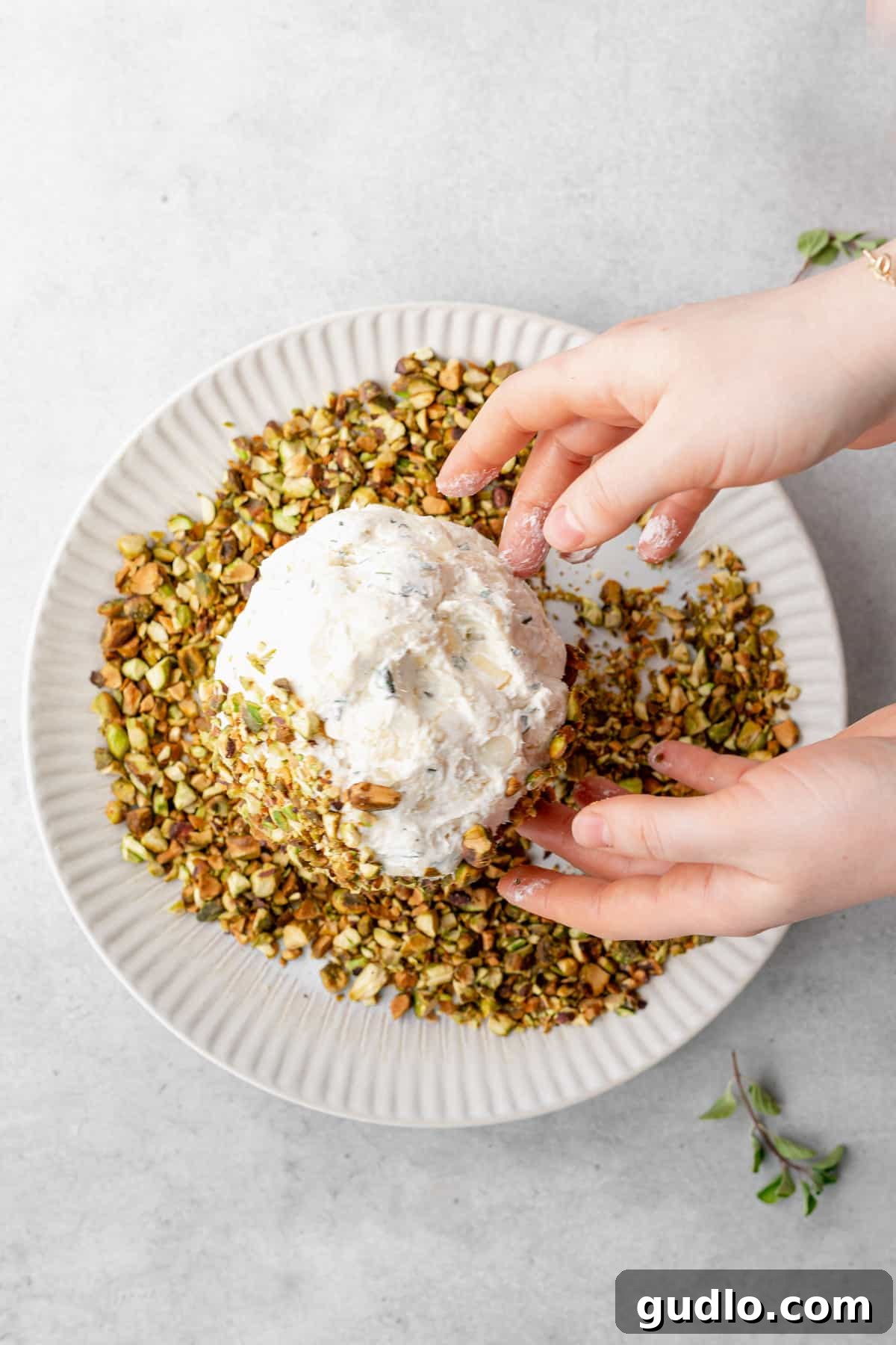 Pistachio Coating Applied to a Fresh Cheese Ball Close-up of a cheese ball being rolled and coated entirely in chopped pistachios.
