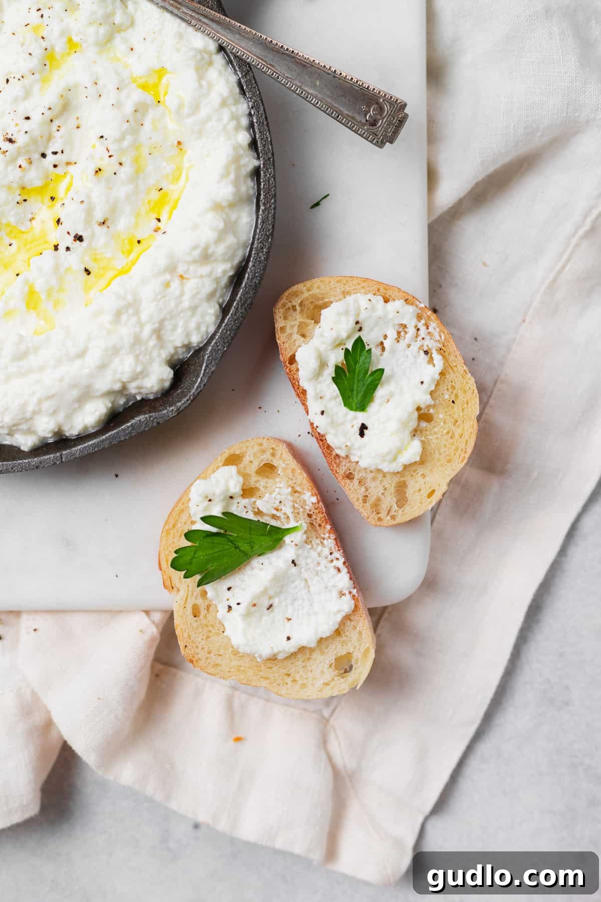 Homemade ricotta cheese is a brilliant way to begin your journey into home cheesemaking. In this post, learn how to make ricotta cheese! Homemade ricotta cheese elegantly served on a piece of crostini, garnished with fresh herbs and a drizzle of olive oil.
