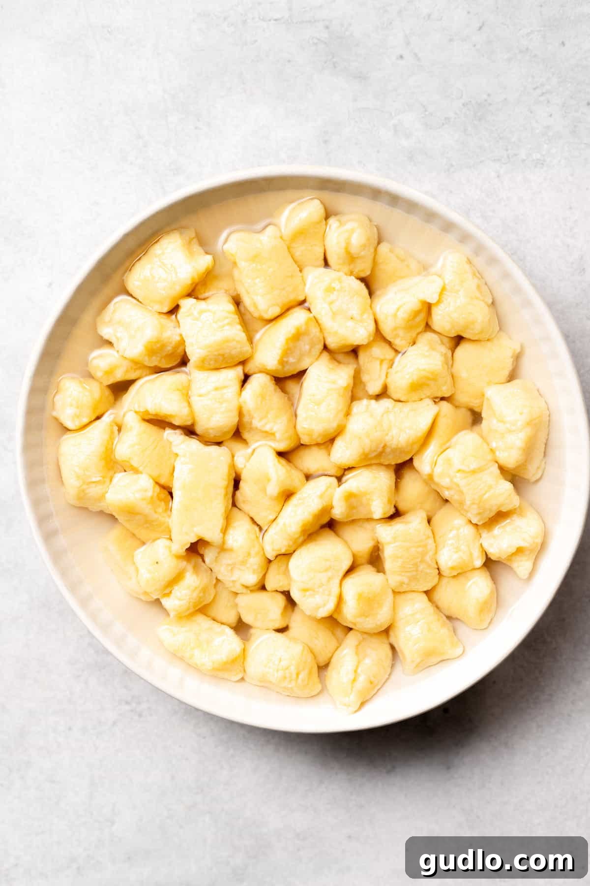 Delicious Homemade Ricotta Gnocchi - A Quick and Easy Italian Classic A bowl of freshly prepared ricotta gnocchi, lightly sauced with a delicate pesto, garnished with fresh herbs and grated cheese, ready to be enjoyed.