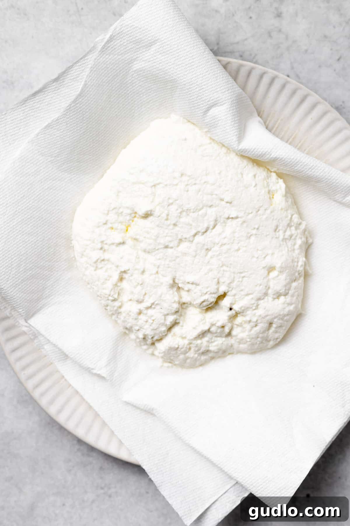 Prepping Ricotta for Perfect Gnocchi Dough Close-up photograph showing ricotta cheese being pressed firmly between layers of paper towels, demonstrating the crucial step of removing excess moisture for optimal gnocchi texture.