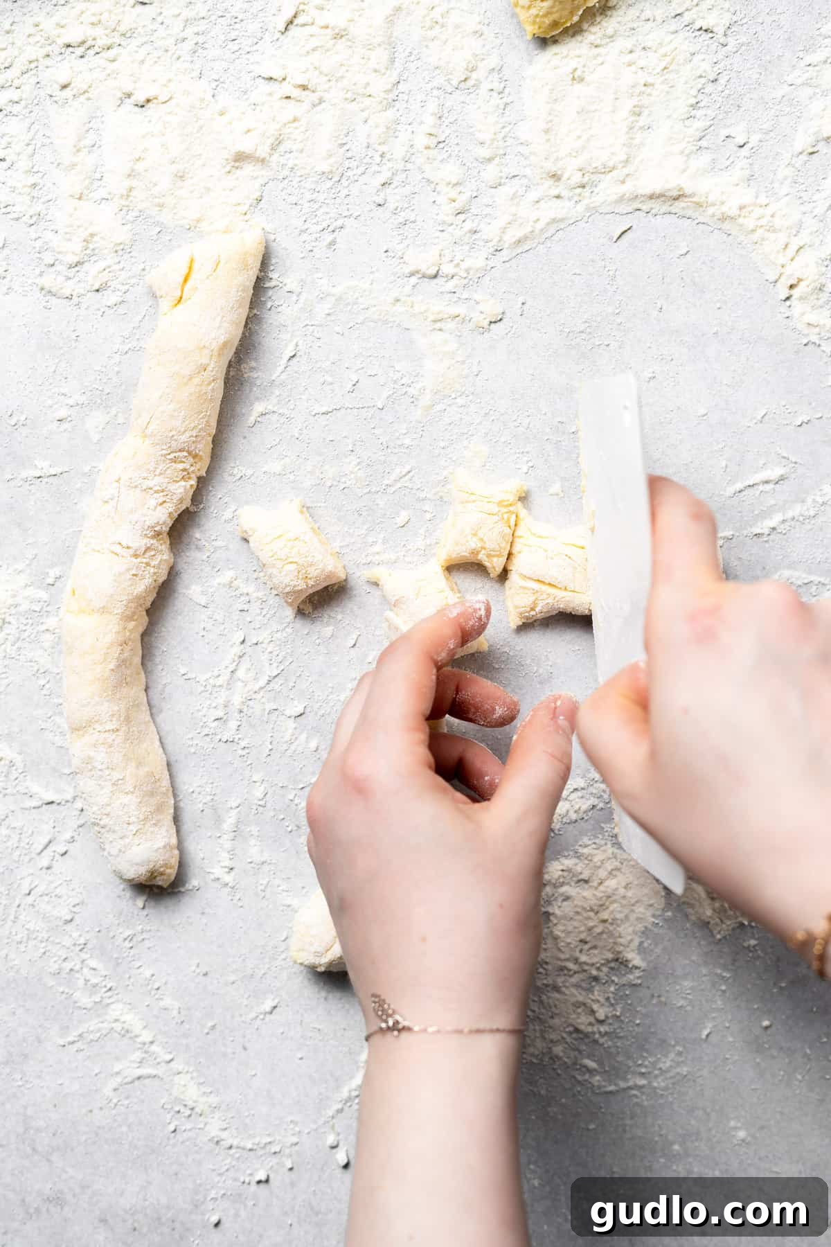 Cutting Gnocchi Pieces for Uniformity Close-up photograph of ricotta gnocchi dough being meticulously cut into uniform bite-sized pieces on a lightly floured surface using a knife, ensuring even cooking.