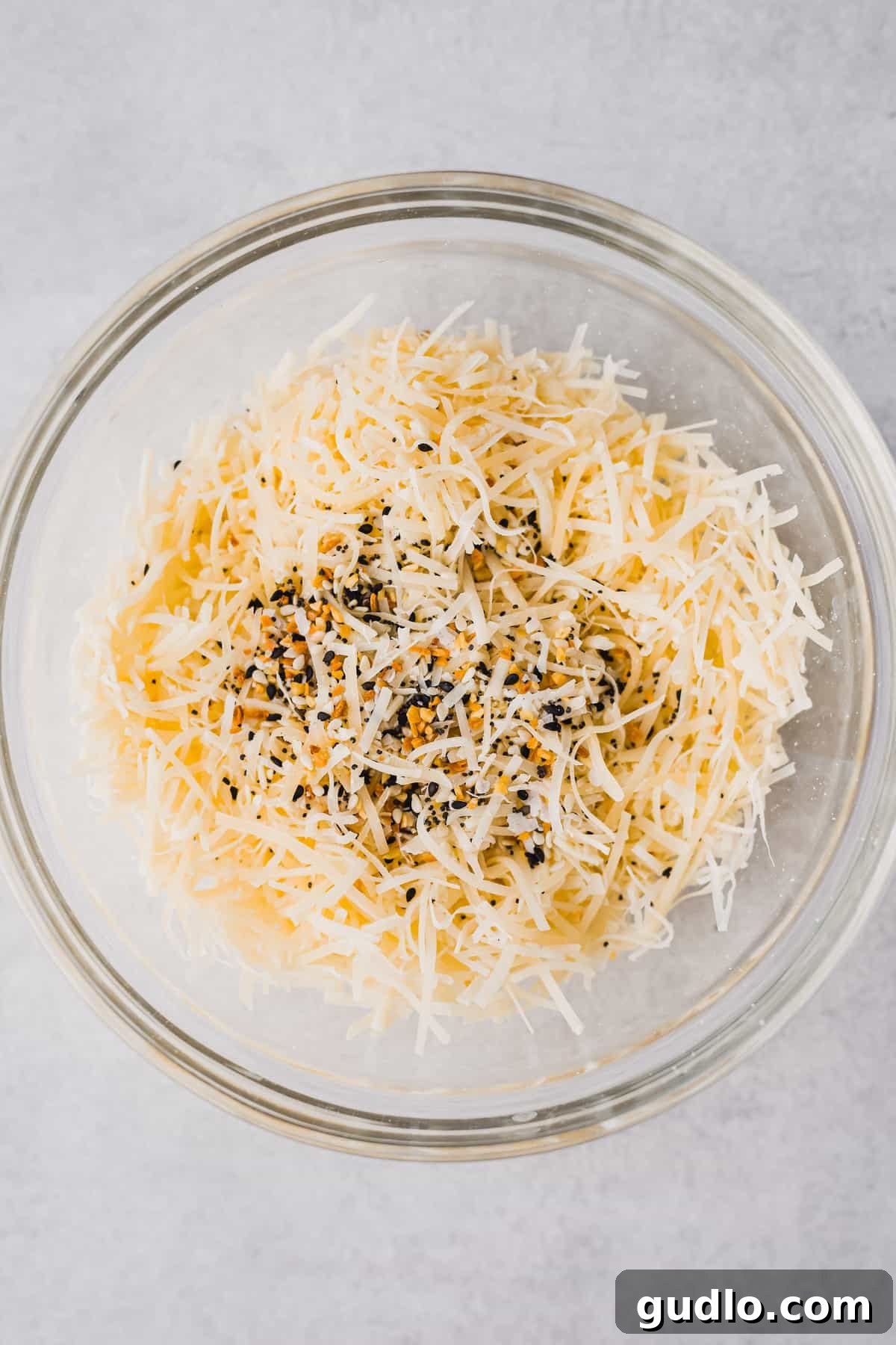 A bowl of freshly shredded parmesan cheese with various spices and herbs, highlighting the simple ingredients for flavorful crisps.