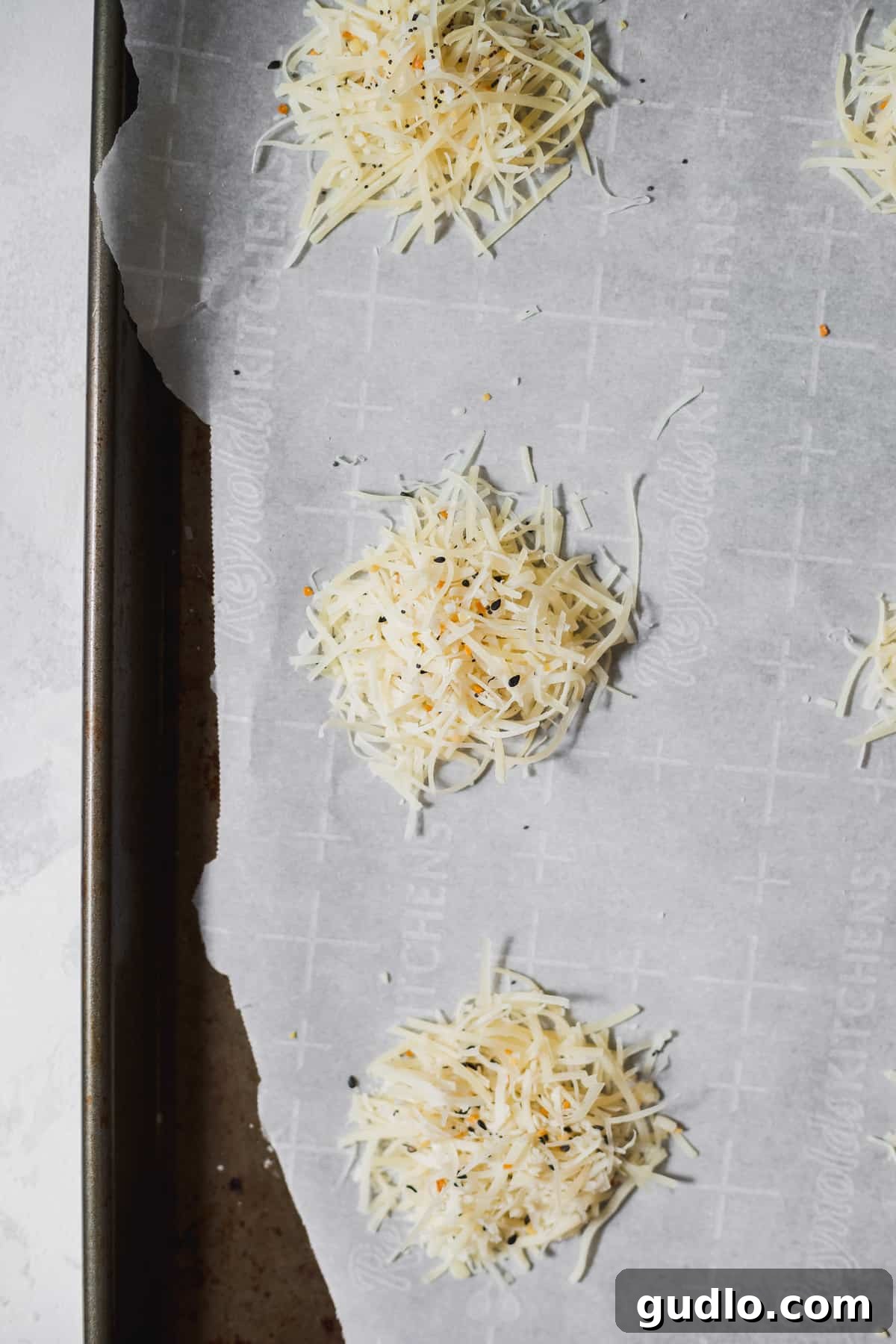 Scooped portions of shredded parmesan cheese seasoned with spices, neatly arranged on a parchment-lined baking sheet before baking.