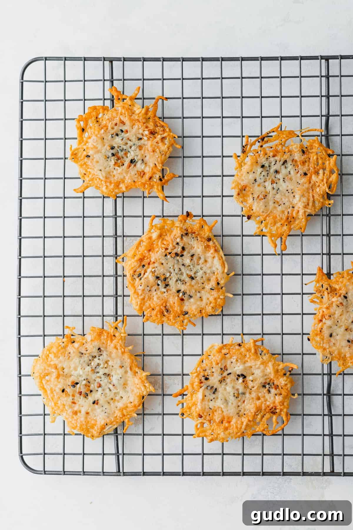 Freshly baked parmesan crisps cooling on a wire rack, achieving their perfect crunchy texture after being removed from the oven.