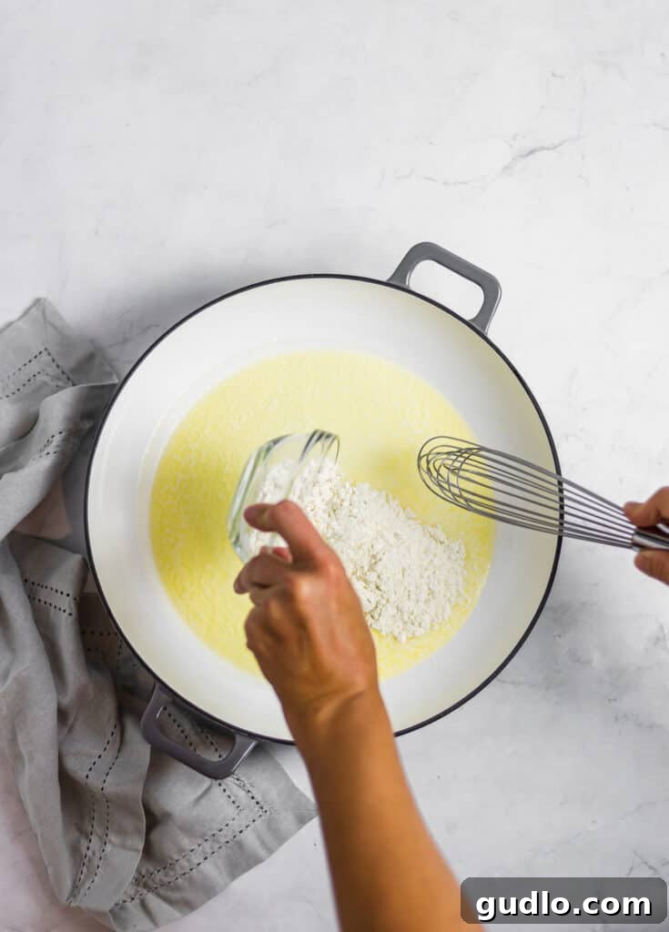 The Definitive Mac and Cheese Sauce 3 Chef whisking melted butter and all-purpose flour vigorously in a hot pan to create a smooth roux base for the creamy cheese sauce