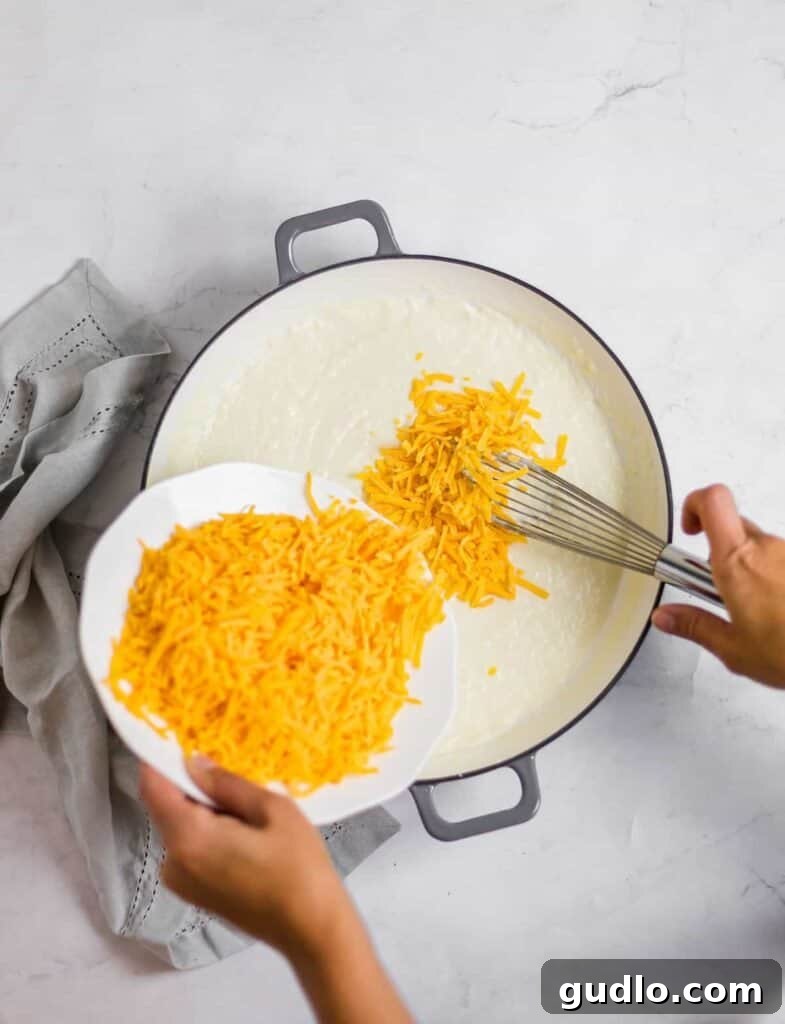 The Definitive Mac and Cheese Sauce 5 Adding generous amounts of freshly shredded sharp cheddar cheese to the steaming hot roux base, preparing to whisk into a smooth sauce