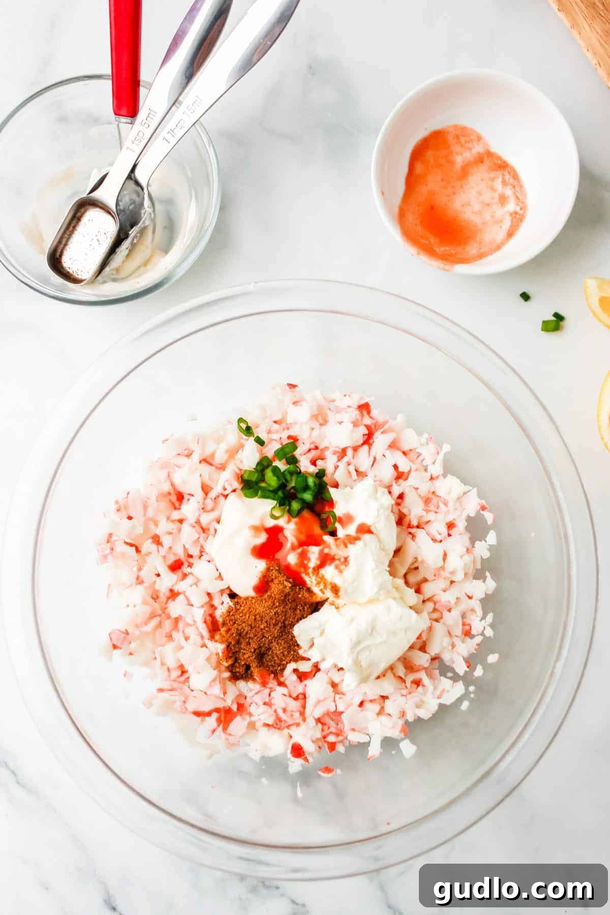 Cool & Creamy Crab Dip 3 All the fresh ingredients for a homemade cold crab dip are laid out in a glass bowl, showcasing their vibrant colors and readiness for mixing.
