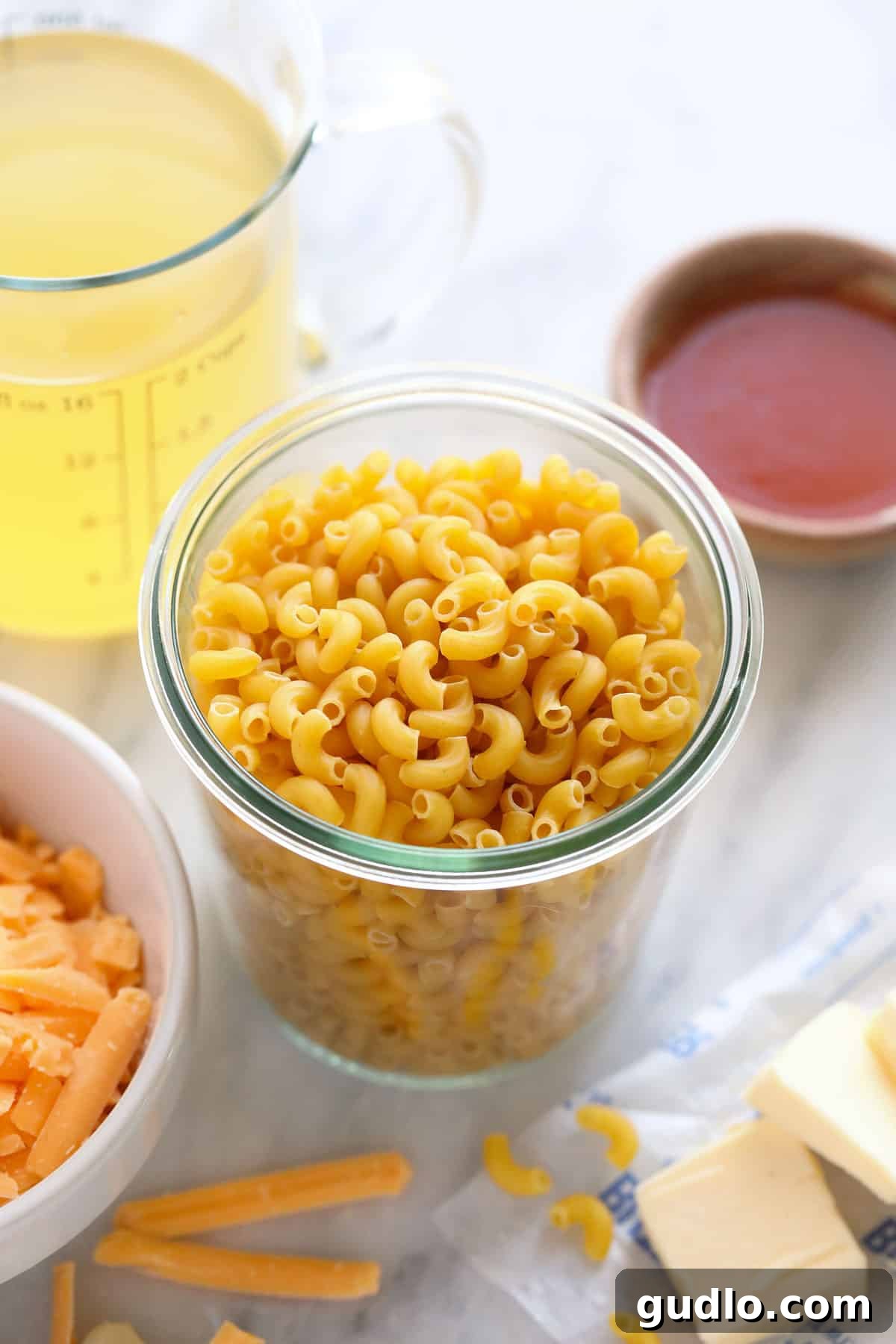 Uncooked elbow macaroni noodles neatly arranged in a clear glass jar, with a wooden spoon, ready for the Instant Pot.