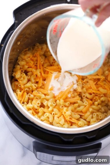 A hand stirring milk, shredded cheese, and hot cooked macaroni in an Instant Pot to create a rich, creamy cheese sauce.
