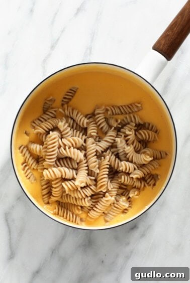 Cooked gluten-free noodles fully coated in a rich, creamy cheese sauce inside a pot, ready to serve.