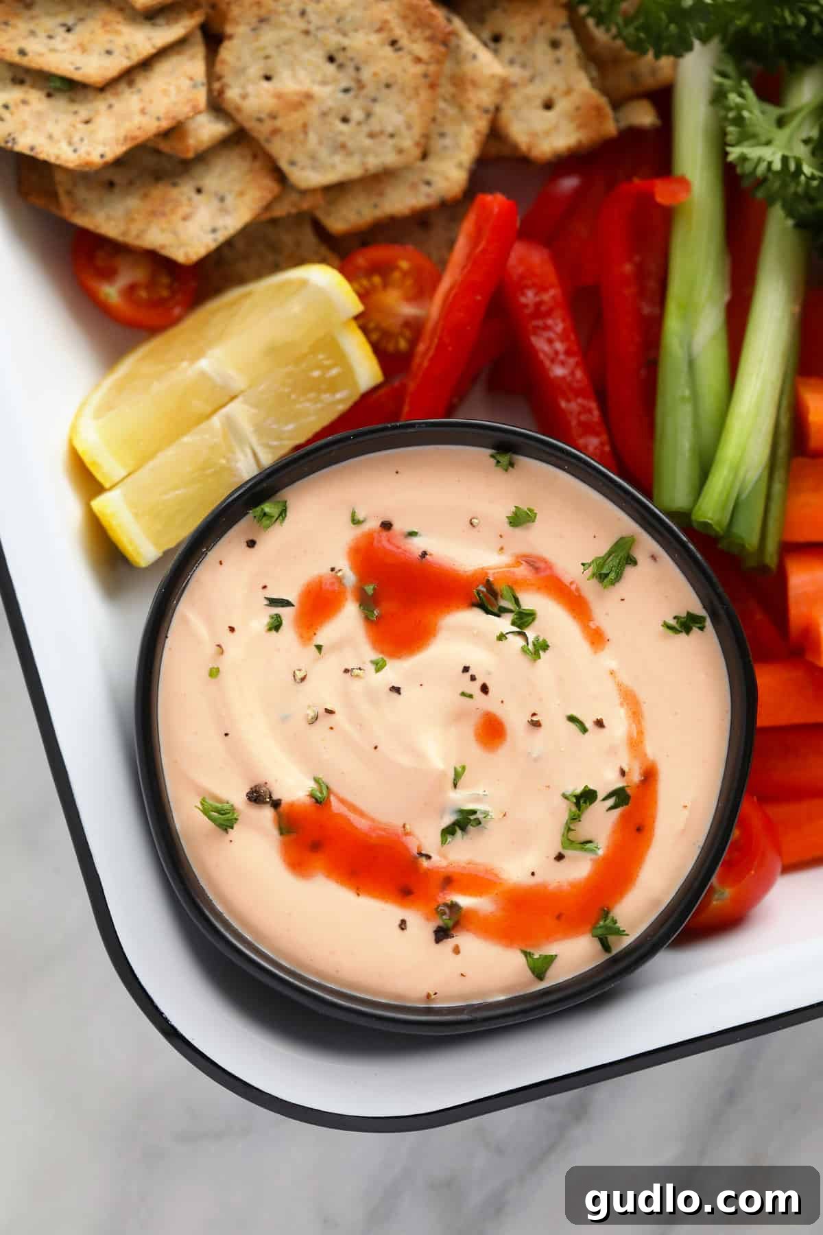 Delicious Buffalo Whipped Cottage Cheese Dip with Dippers A bowl of creamy Buffalo Whipped Cottage Cheese Dip, garnished with cracked black pepper, surrounded by a vibrant selection of fresh vegetables like carrots, celery, bell peppers, and crispy crackers for dipping.