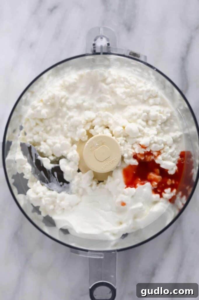 Dairy Ingredients in Food Processor for Whipped Dip The initial dairy ingredients – full-fat cottage cheese, Greek yogurt, and softened cream cheese – placed inside a high-speed food processor, ready to be blended into a smooth base.