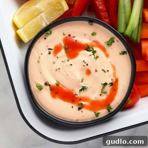 A bowl of Buffalo Whipped Cottage Cheese Dip, elegantly garnished with a light sprinkle of cracked pepper, poised on a wooden surface and ready for serving with a spread of delicious dippers.