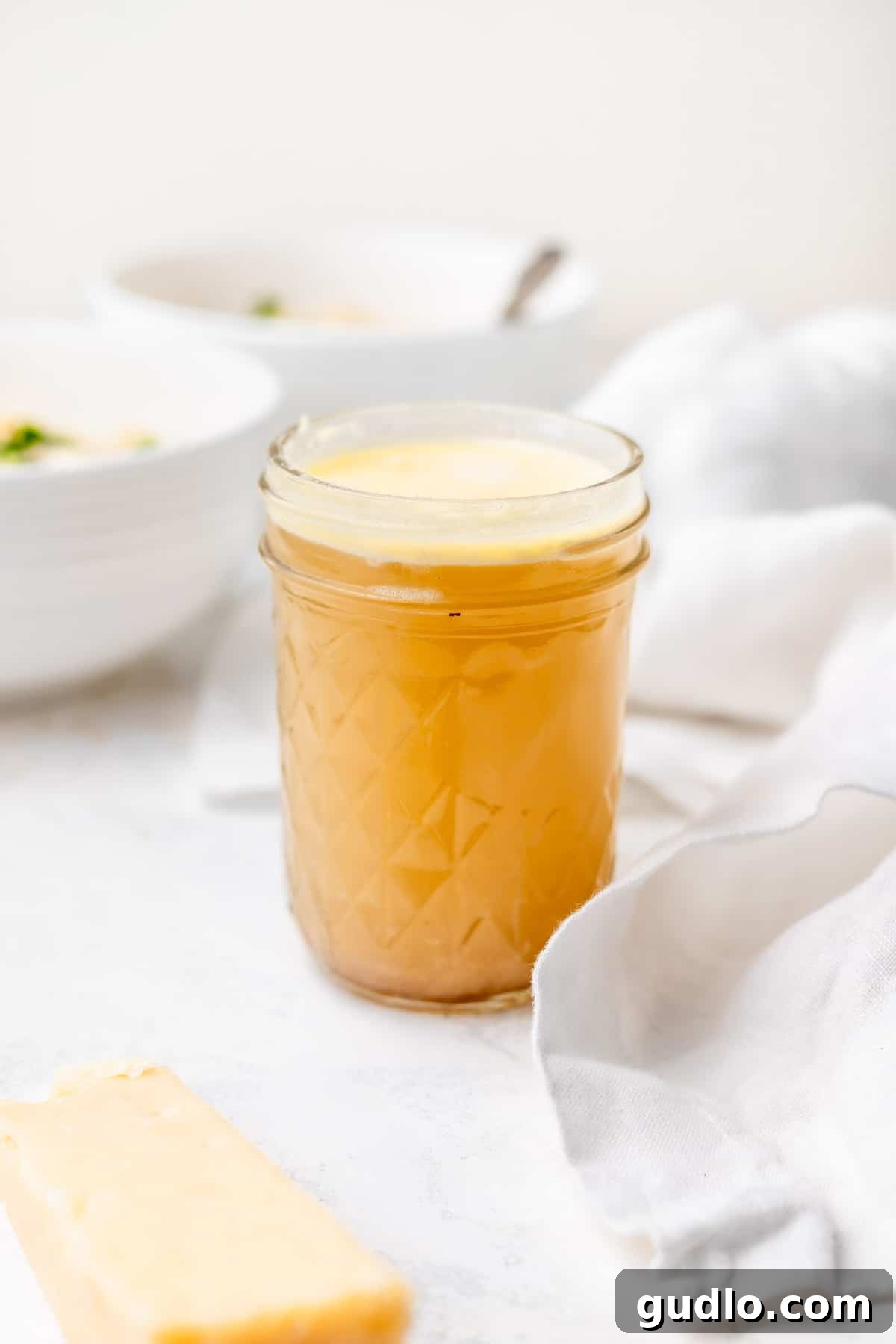 Stored Parmesan Broth A glass jar filled with golden homemade parmesan broth, garnished with a sprig of fresh thyme, set against a rustic background.