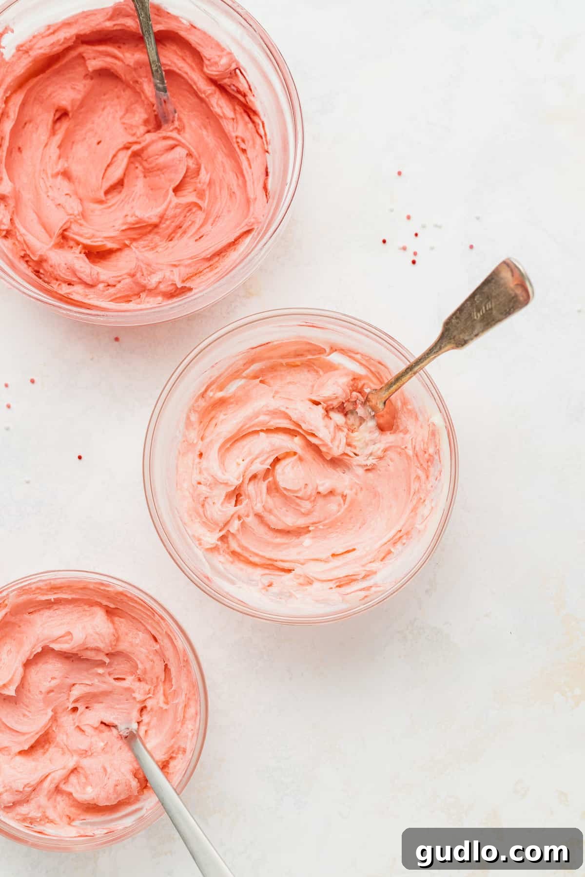 The Easiest & Most Delicious Cream Cheese Frosting for Sugar Cookies Two aesthetically arranged bowls showcasing fluffy, vibrant cream cheese frosting in different colors, ready to be used for decorating sugar cookies.