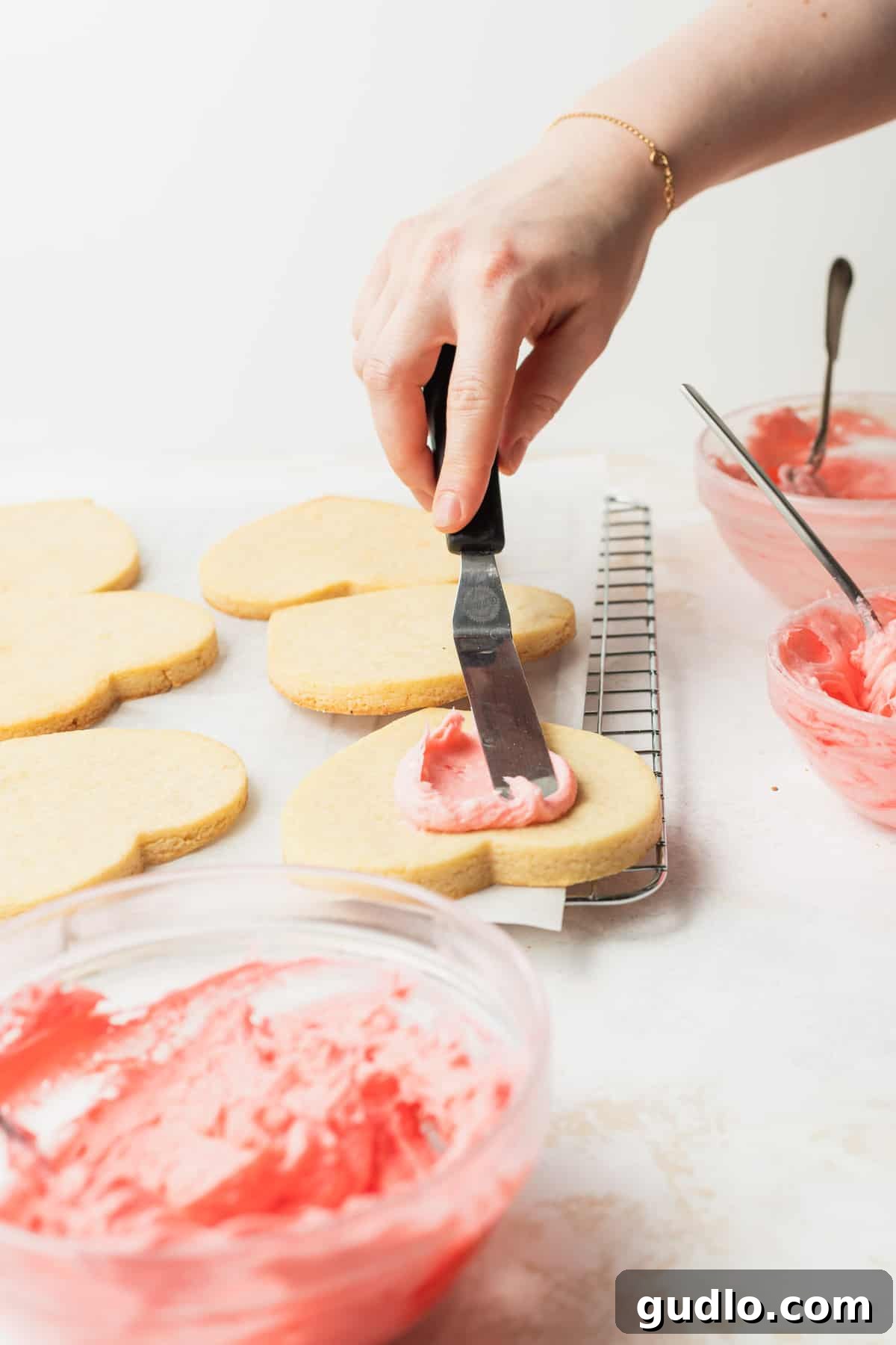 Decorating Sugar Cookies with Delicious Cream Cheese Frosting Hands carefully decorating a vibrant red sugar cookie with white cream cheese frosting and colorful sprinkles, showcasing the final step of creation.