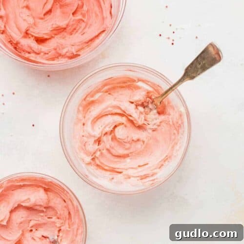 Two small bowls of cream cheese frosting, one pristine white and another tinted a soft pink, perfectly set for cookie decoration.