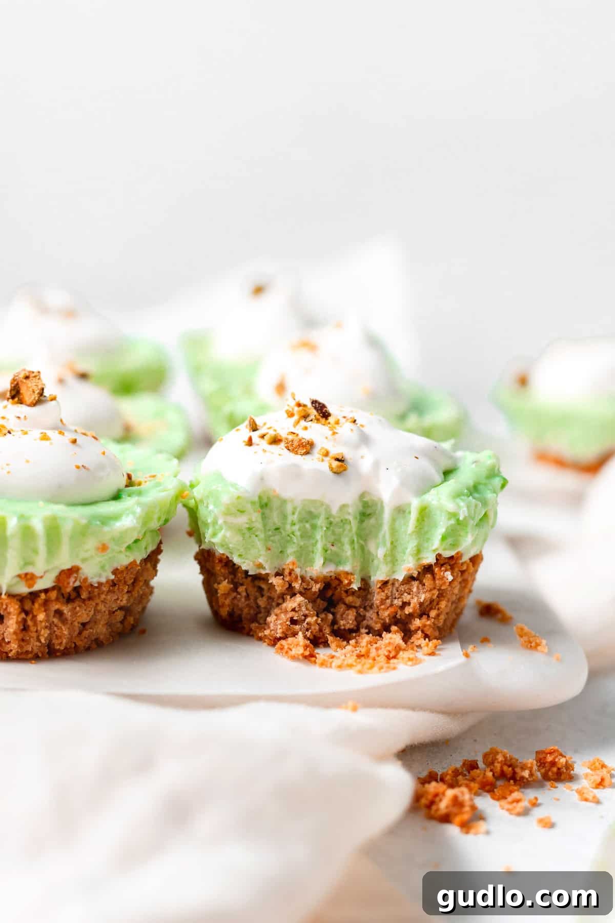 These pistachio pie cups are an individual size pistachio pie you'll absolutely LOVE! Made with a pistachio cheesecake filling and an easy graham cracker crust. Don't forget the dollop of whip on top! Pistachio pie cups with a bite taken out of one of them, showcasing the creamy green filling and golden crust.