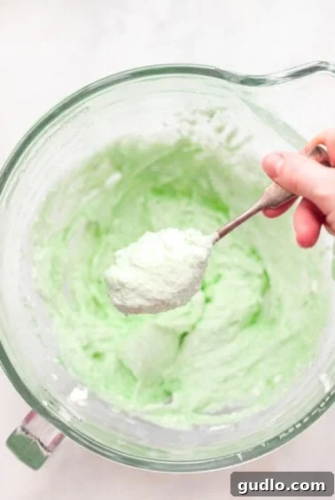 A person mixing green pistachio frosting in a bowl, demonstrating the texture.