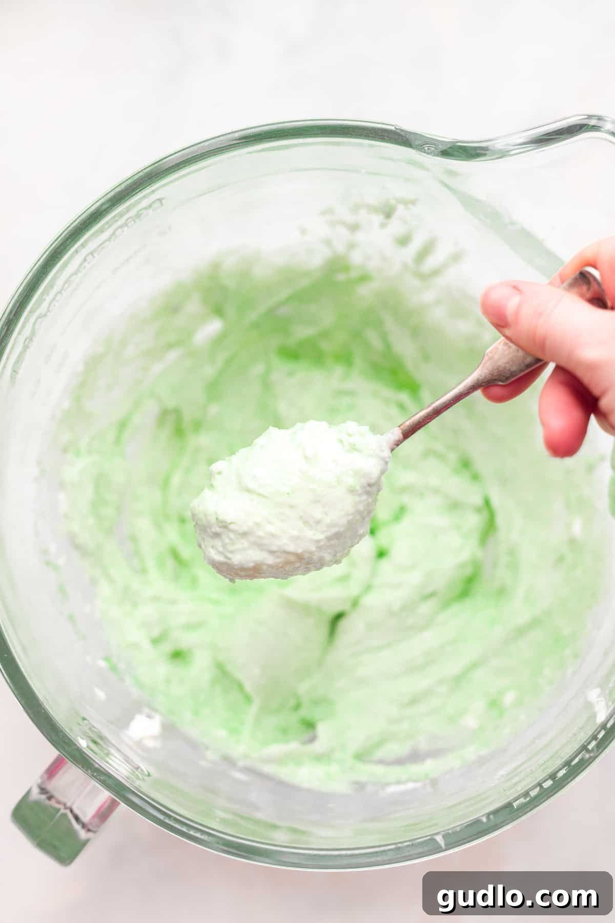 Pistachio pie filling on a spoon, ready to be dolloped into pistachio pie cups. Pistachio pie filling on a spoon, ready to be dolloped into graham cracker crusts, showing its smooth, creamy texture.