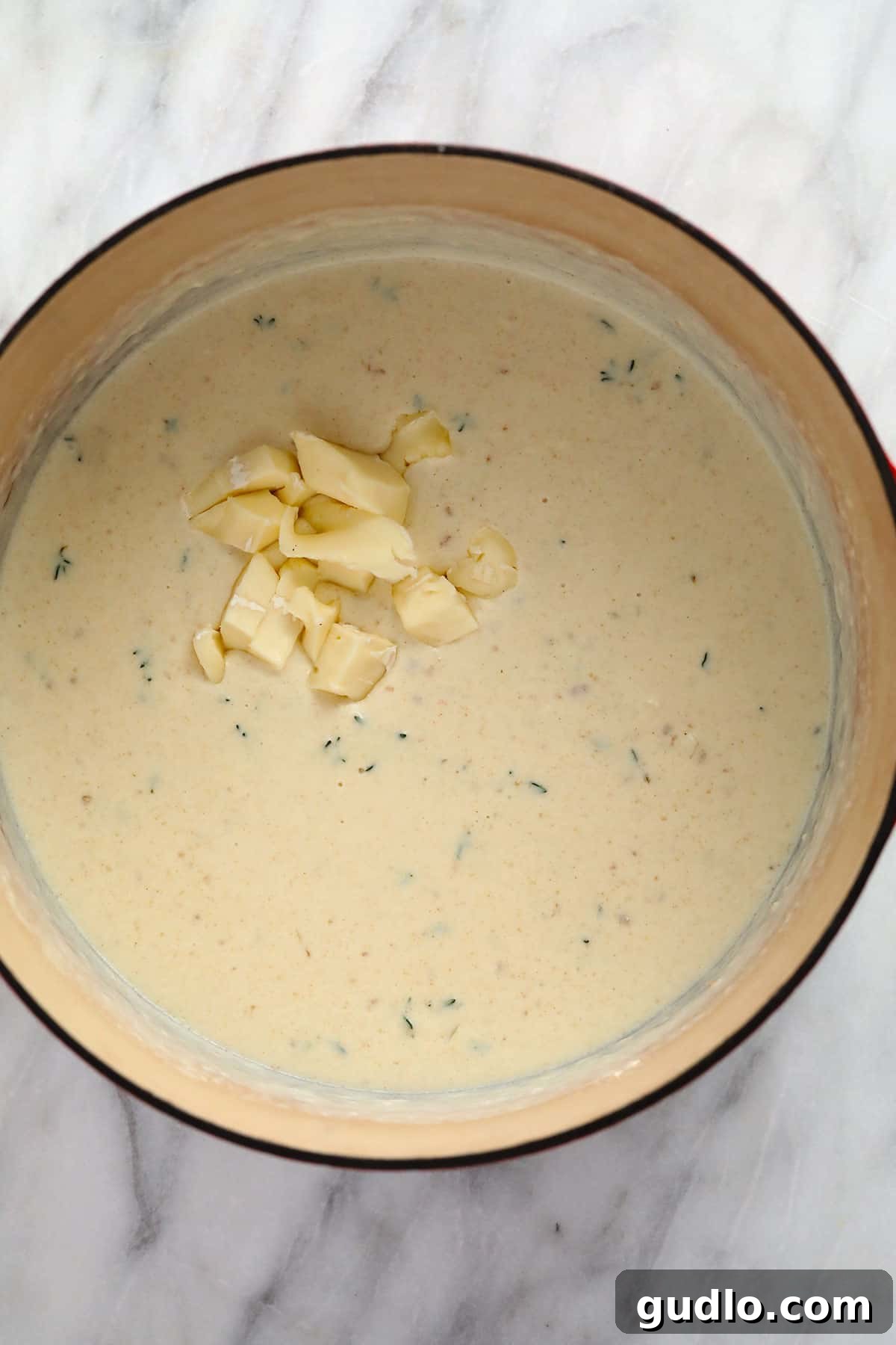 Cubed brie cheese melting into a thick and creamy roux in a saucepan.