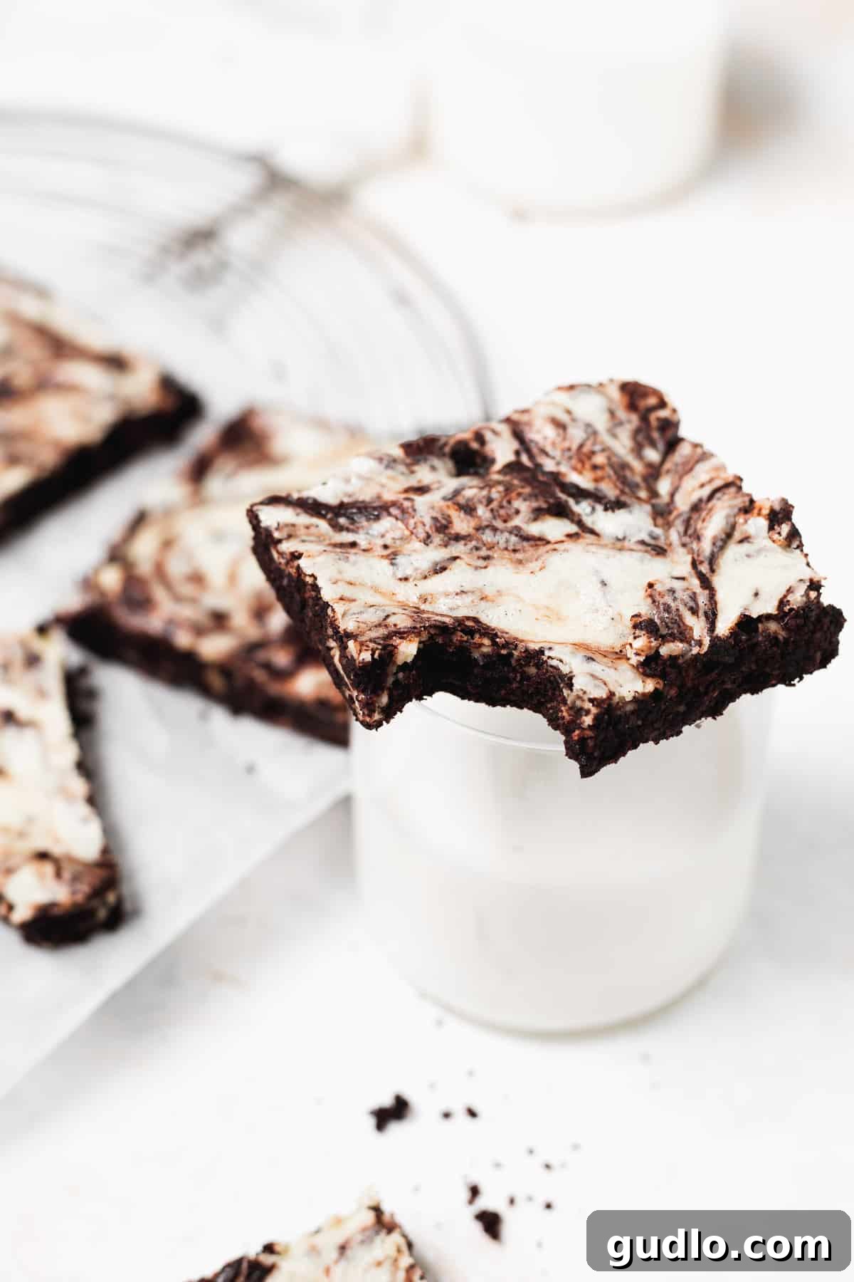 Decadent Cream Cheese Swirl Brownies 7 A cream cheese brownie delicately balanced on the rim of a glass of milk.