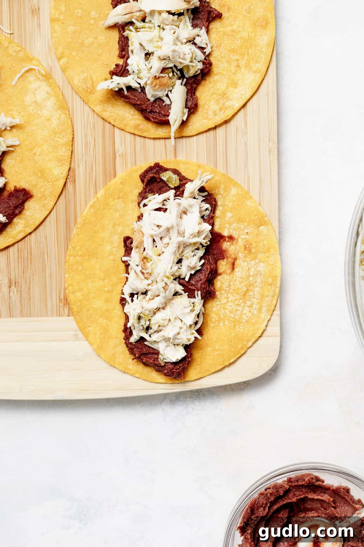 Comforting Homestyle Chicken Enchiladas 3 Warm corn tortillas being filled with a flavorful mixture of seasoned shredded chicken and creamy refried black beans, preparing for rolling.