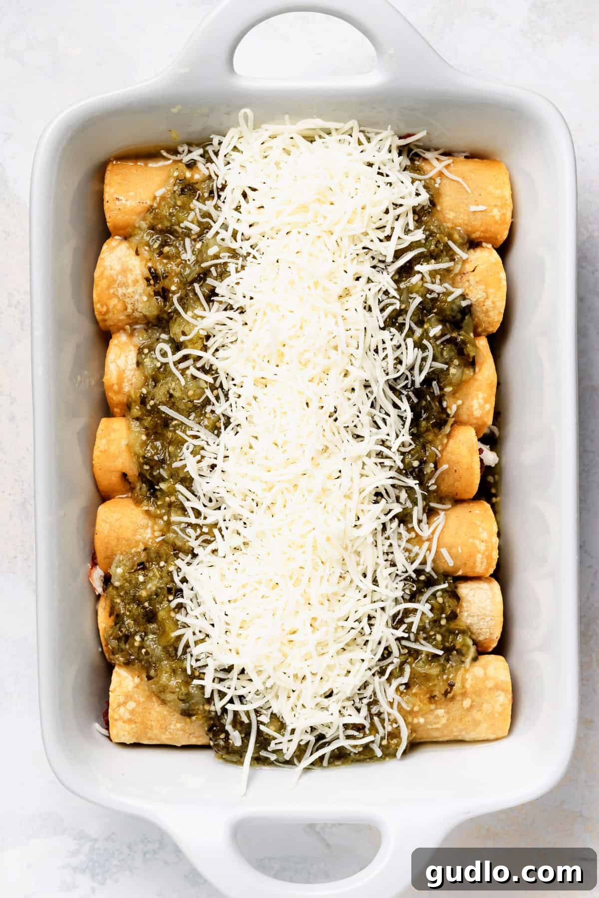 Comforting Homestyle Chicken Enchiladas 5 Freshly baked enchiladas nestled in a casserole dish, generously sprinkled with melted Monterey Jack cheese and ready for final garnishes.
