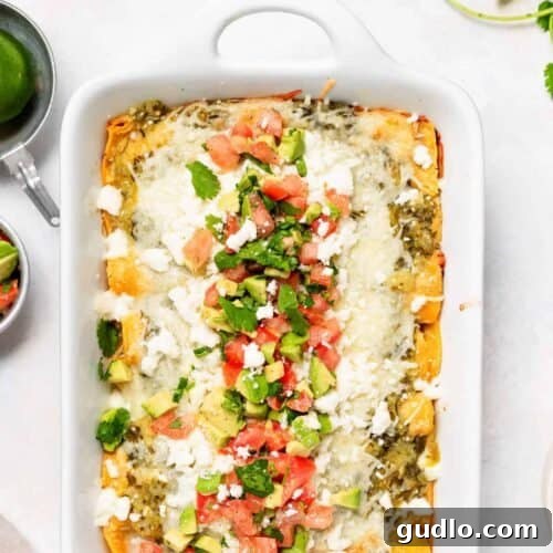 A casserole dish filled with baked chicken enchiladas, topped with vibrant green salsa and melted cheese.