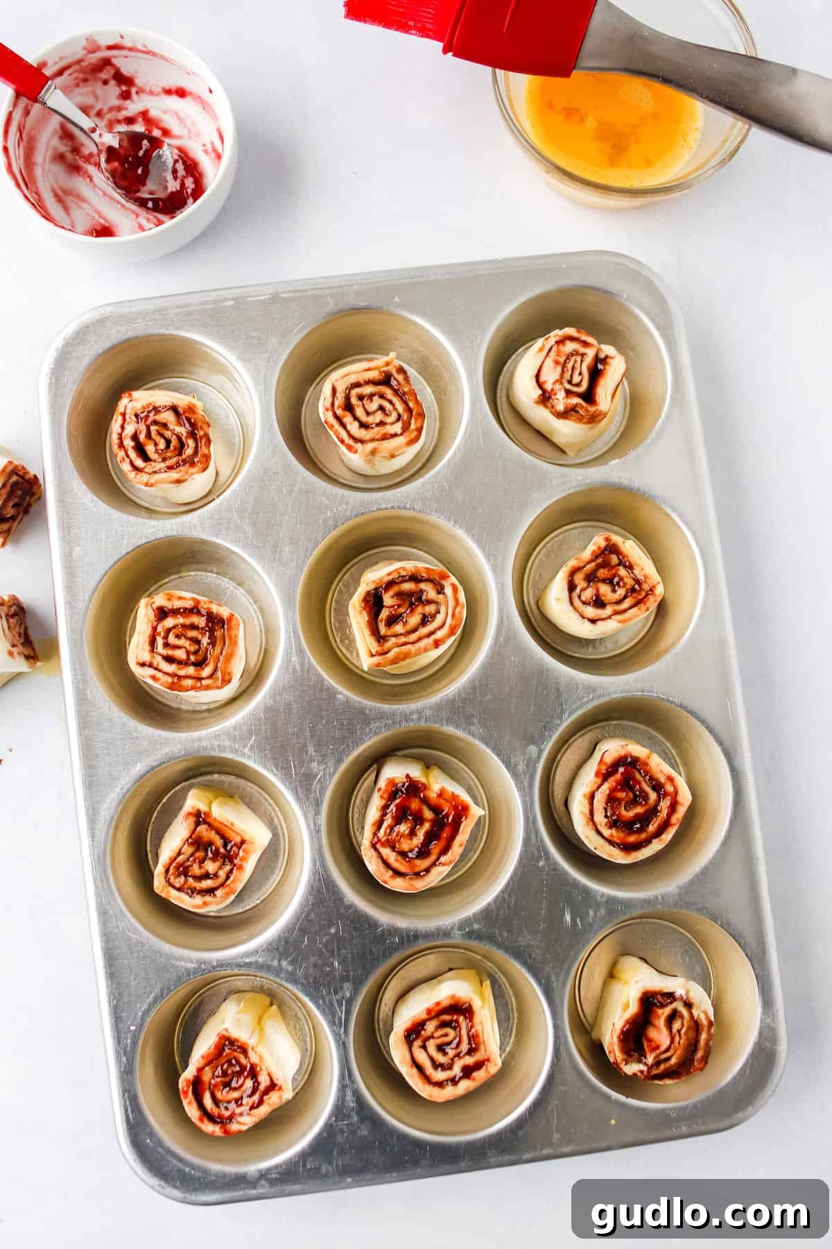 Start your day with these delicious Chocolate Raspberry Cinnamon Rolls that use store-bought dough and a few simple ingredients paired with a delicious cream cheese glaze. Unbaked Chocolate Raspberry Cinnamon Rolls neatly arranged in a greased muffin tin, clearly showing their intricate spiral layers, eagerly awaiting their delicious transformation in the preheated oven.