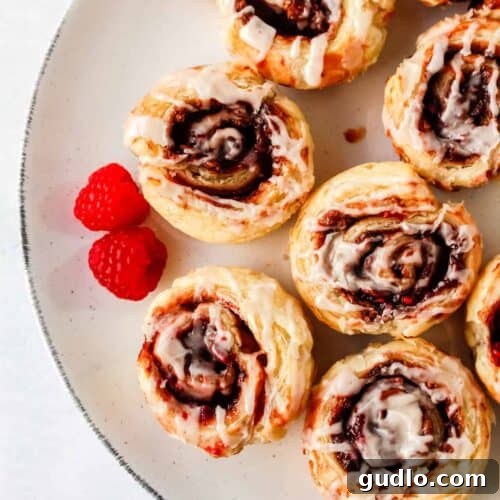 Close-up of a perfectly baked Chocolate Raspberry Cinnamon Roll, glistening with cream cheese glaze, ready to be served and enjoyed as a delightful breakfast or dessert.