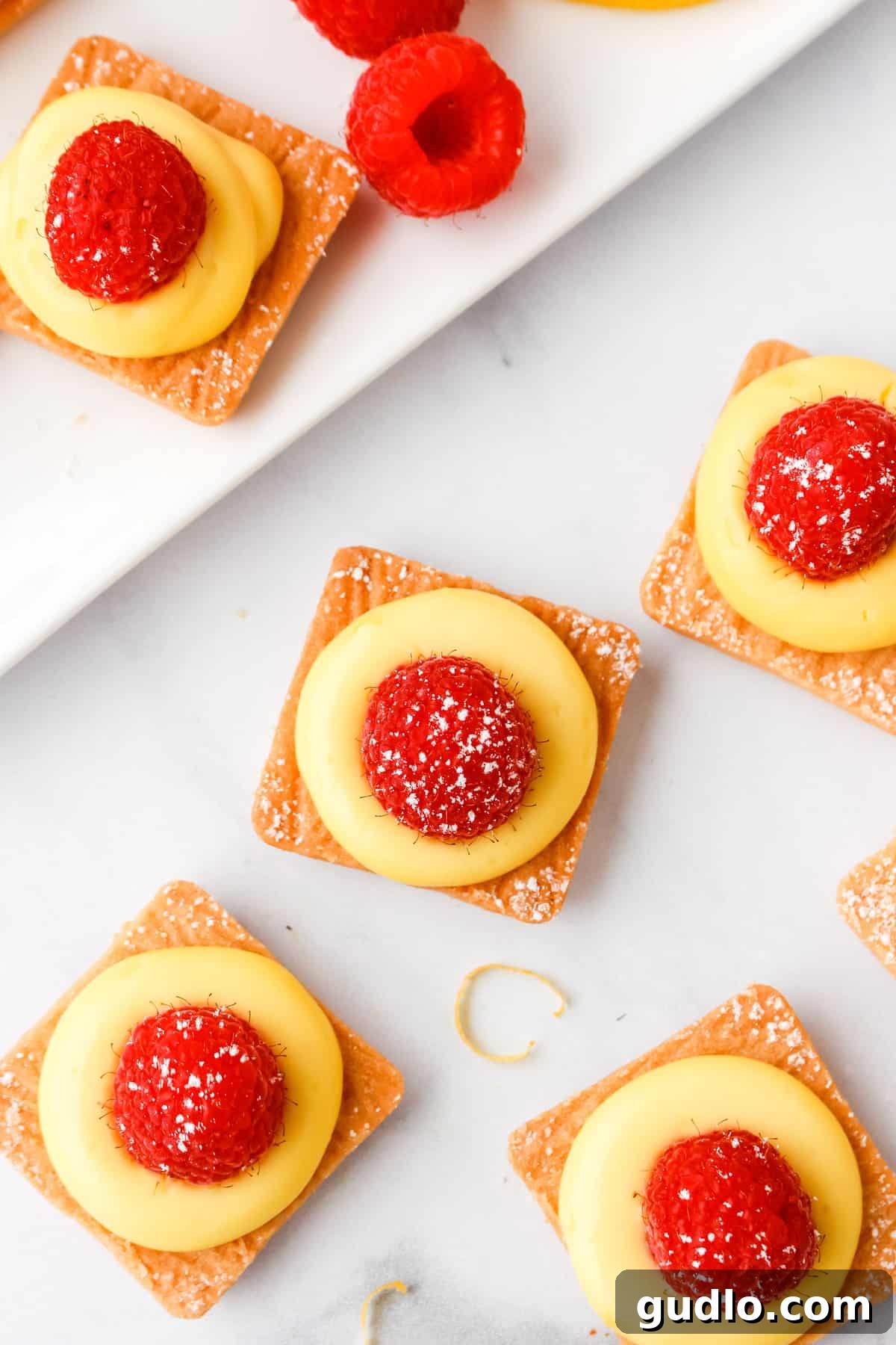 no-bake lemon cheesecake bites on plate, garnished with fresh raspberries