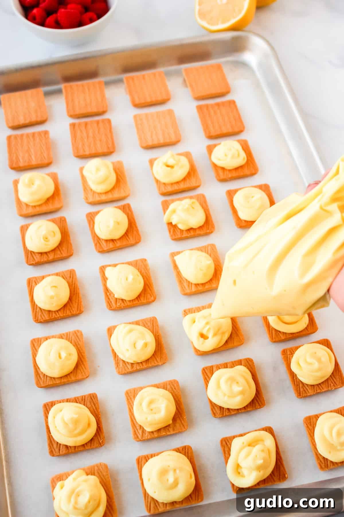piping lemon filling onto shortbread cookies on a baking sheet