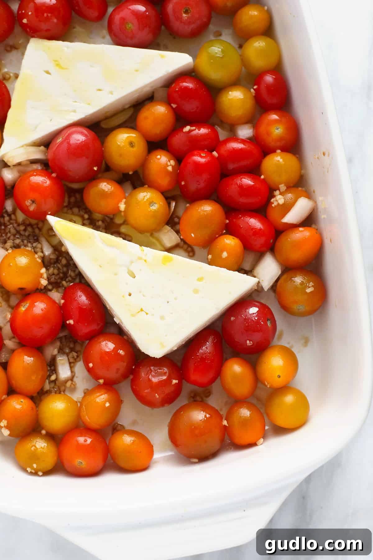 Feta cheese with tomatoes and garlic, pre-baking. Close-up of a block of feta cheese nestled among bright cherry tomatoes and minced garlic in a baking dish, ready for the oven.