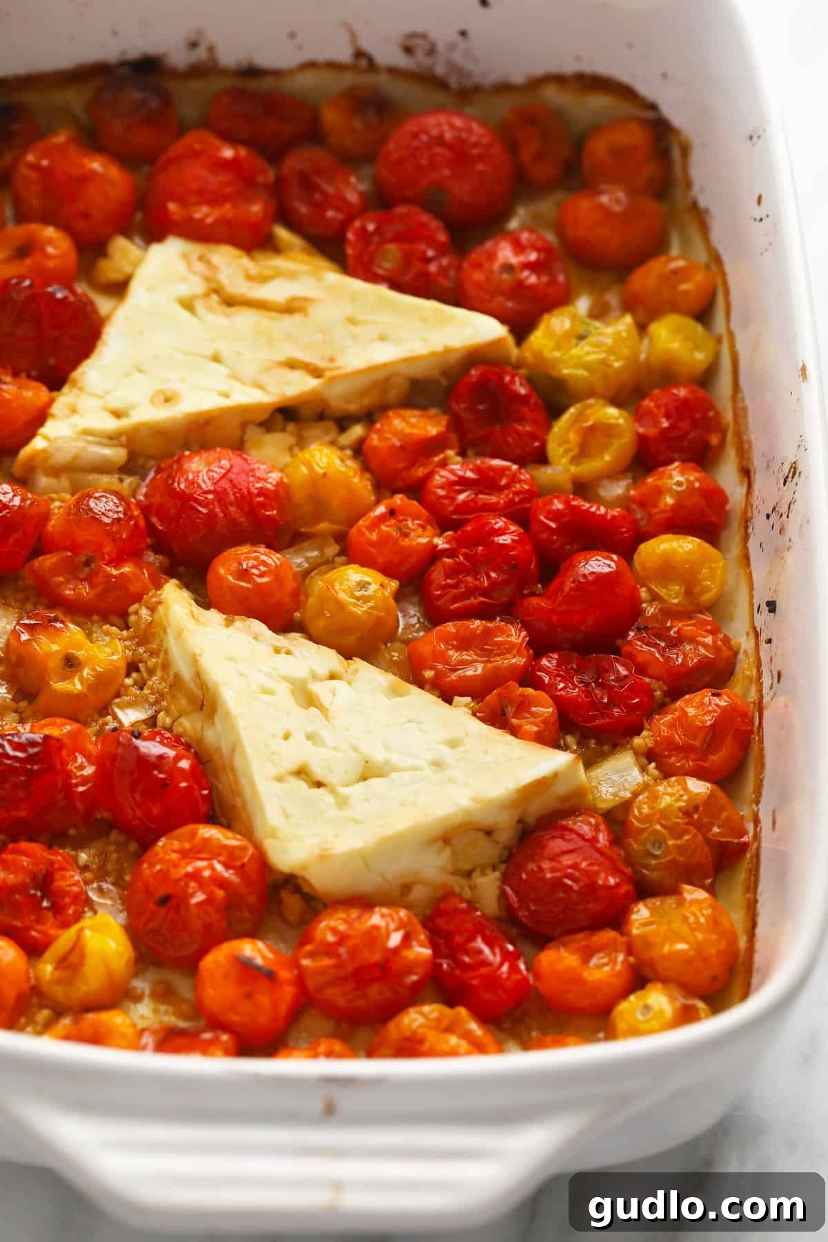 Roasted tomatoes and feta cheese, freshly out of the oven. Perfectly roasted cherry tomatoes and a melted block of feta cheese, bubbling hot in a baking dish, ready to be mashed into a sauce.
