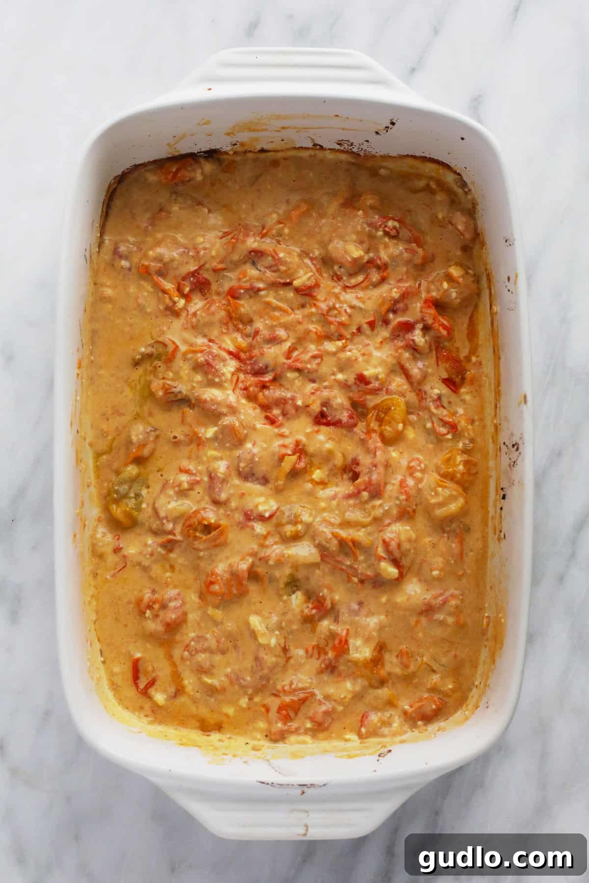 Creamy feta pasta sauce, freshly prepared in the baking dish. Creamy, blended feta pasta sauce with burst tomatoes and melted feta, perfectly mixed in the casserole dish before adding pasta.