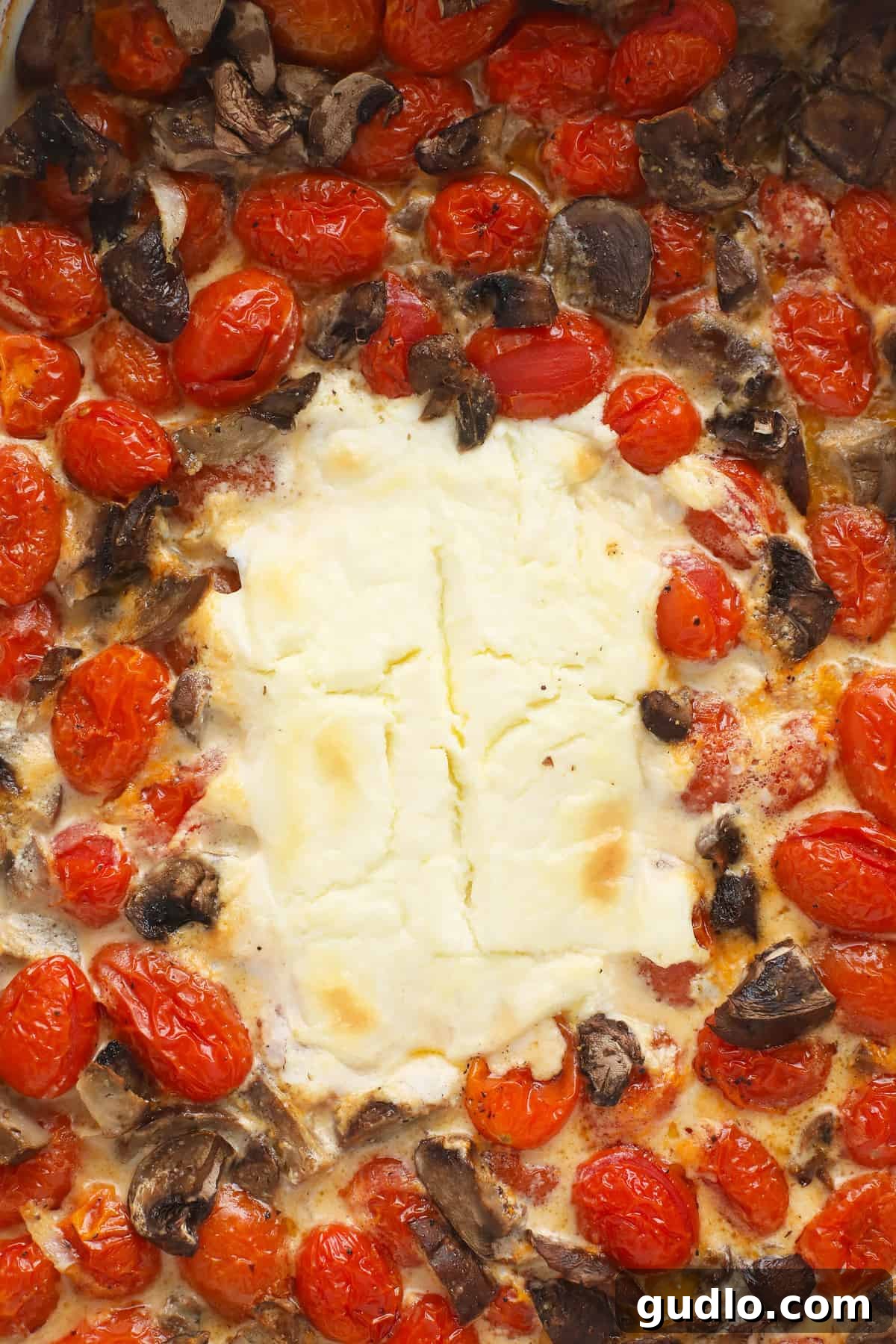 Baked Cream Cheese with Roasted Vegetables A block of baked cream cheese surrounded by perfectly roasted cherry tomatoes and tender mushrooms in a casserole dish, ready for mashing and mixing.
