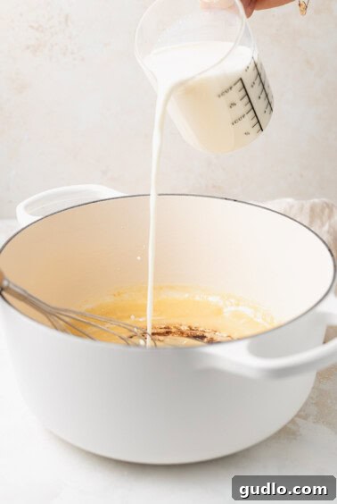 A person making white cheddar mac and cheese by pouring milk into a pan.