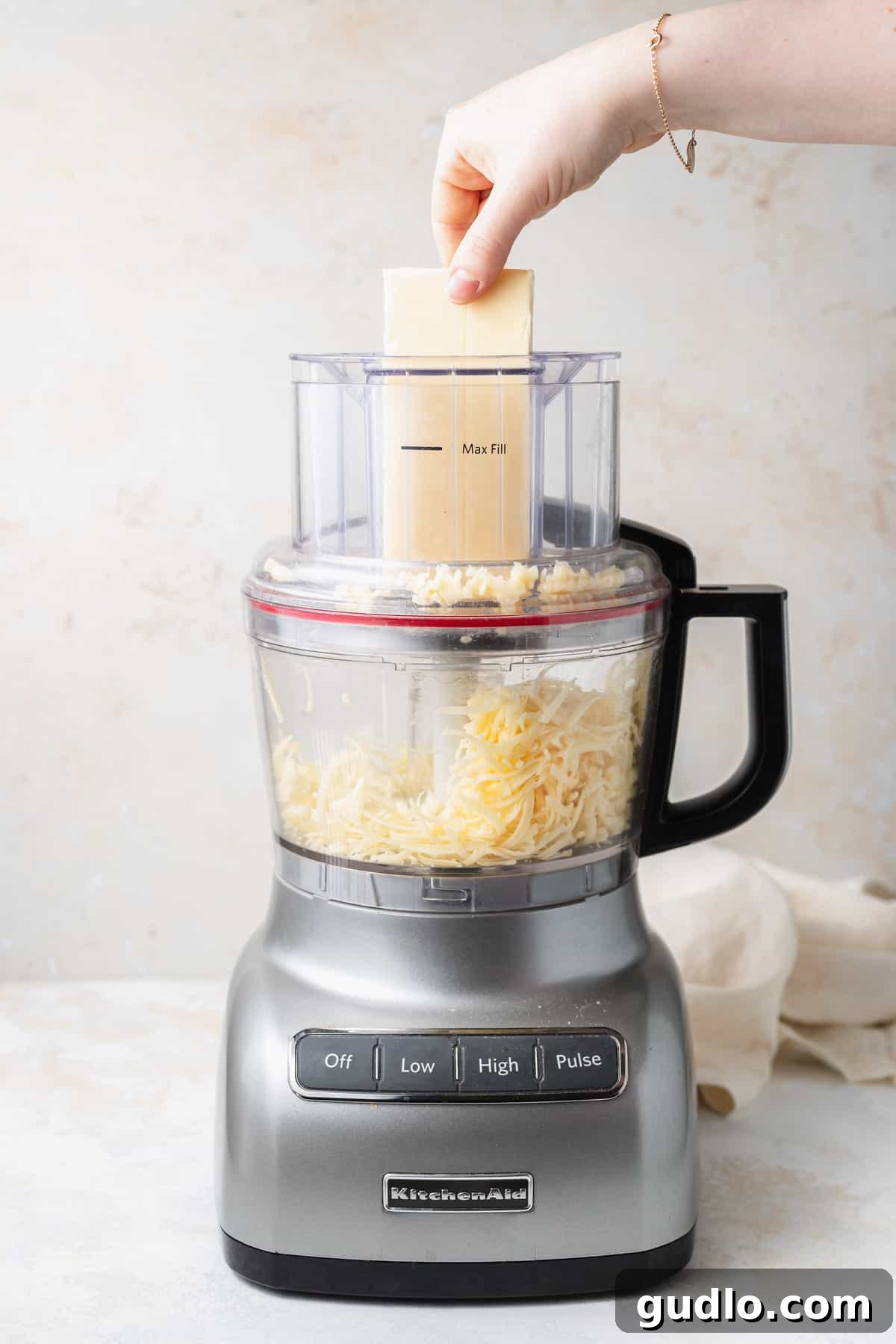 Hands grating fresh white cheddar cheese using a food processor for the mac and cheese recipe.