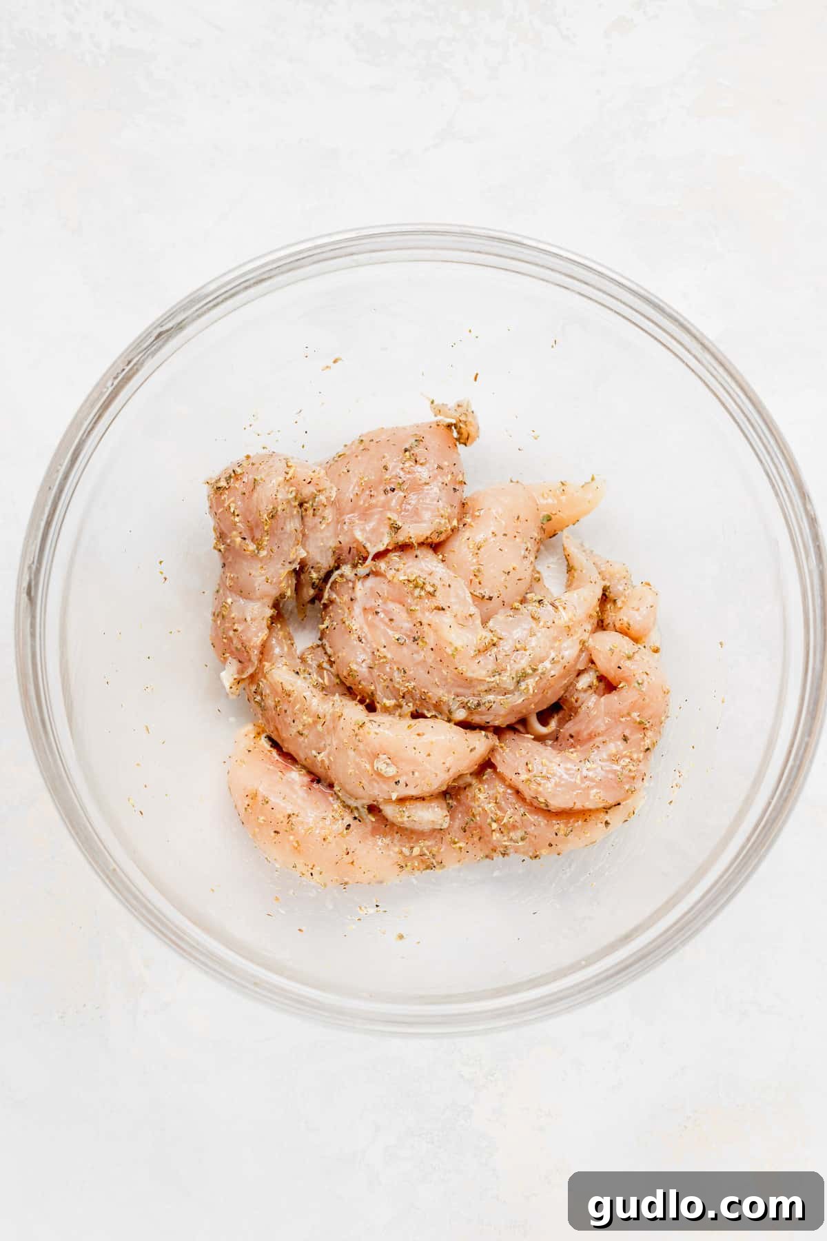 Sheet Pan Mediterranean Chicken Gyros 3 Chicken tenderloin strips in a bowl, seasoned with spices and lemon zest, ready for marinating.