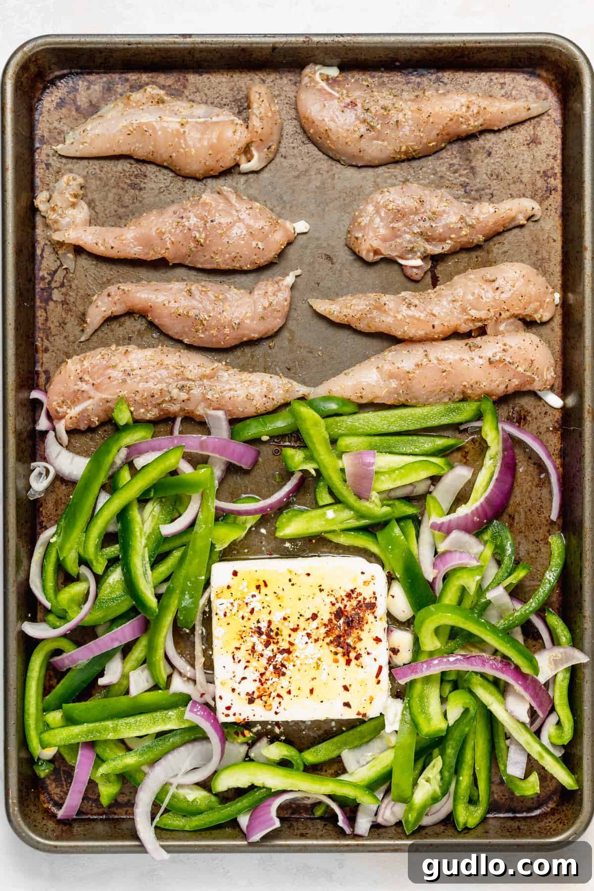 Sheet Pan Mediterranean Chicken Gyros 4 Chicken, roasted bell peppers, onions, and a block of feta cheese baking together on a single sheet pan.