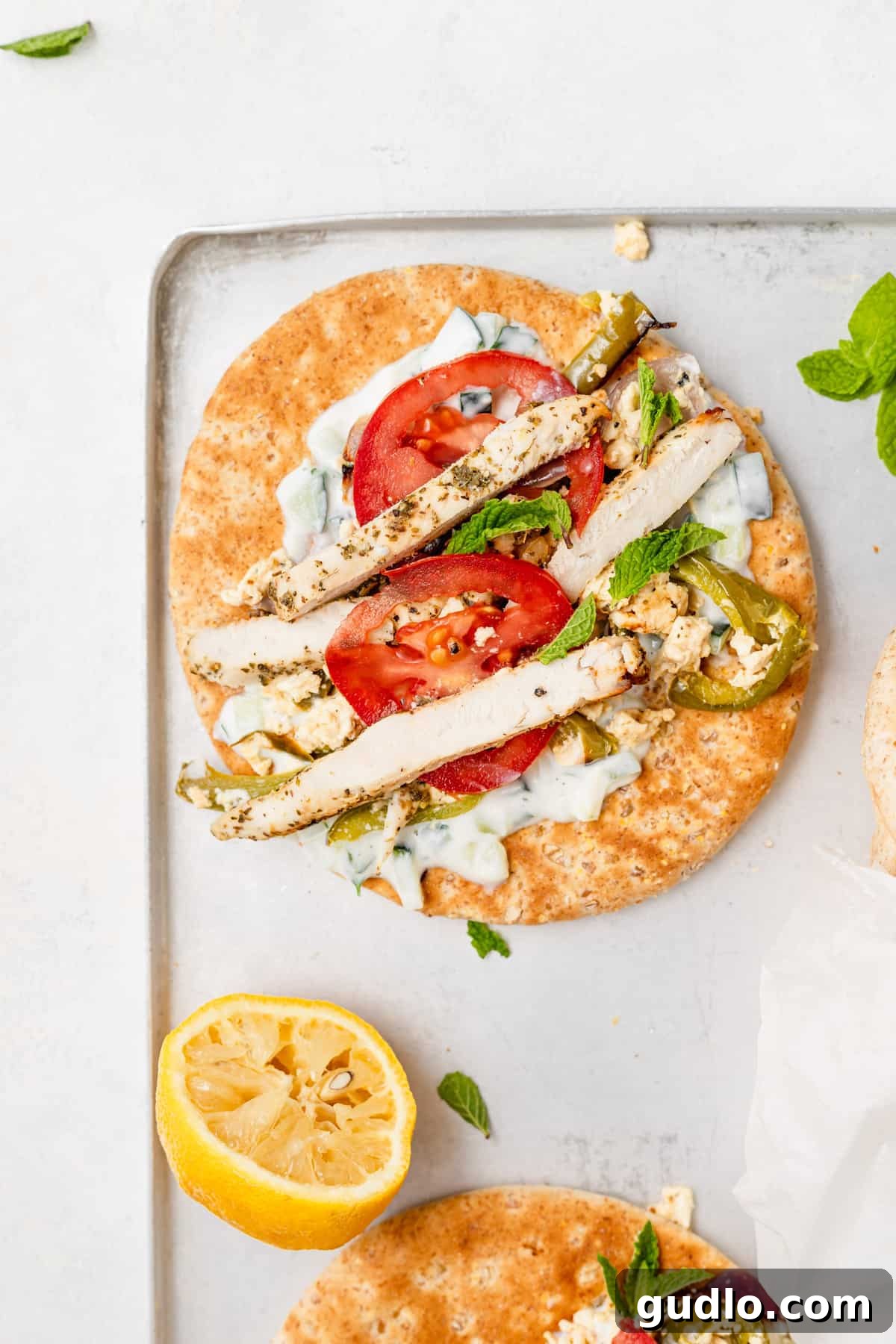 Sheet Pan Mediterranean Chicken Gyros 6 Multiple assembled chicken gyros, wrapped in parchment paper, presented beautifully on a sheet pan.