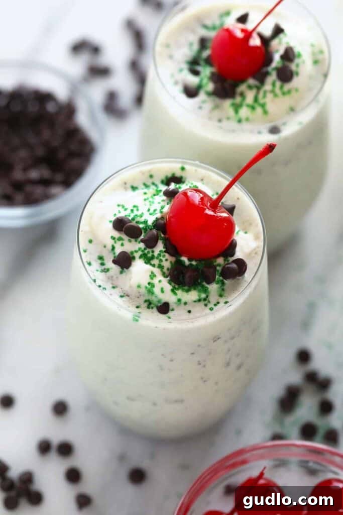Creamy Mint Shamrock Shake 2 A vibrant green Shamrock Shake in a clear glass, topped generously with fluffy white whipped cream, a bright red maraschino cherry, and festive green sprinkles, perfectly ready to be enjoyed.