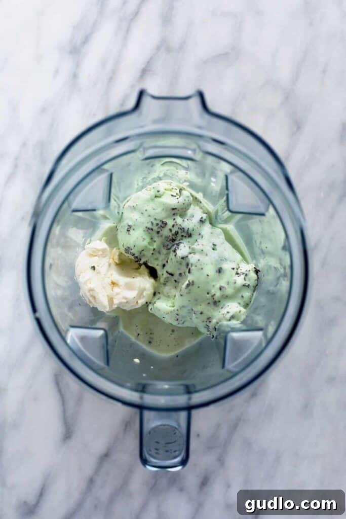 Creamy Mint Shamrock Shake 4 The key ingredients for a Shamrock Shake, including mint chip ice cream, milk, cream cheese, and peppermint extract, are being added to a high-speed blender, ready for mixing.
