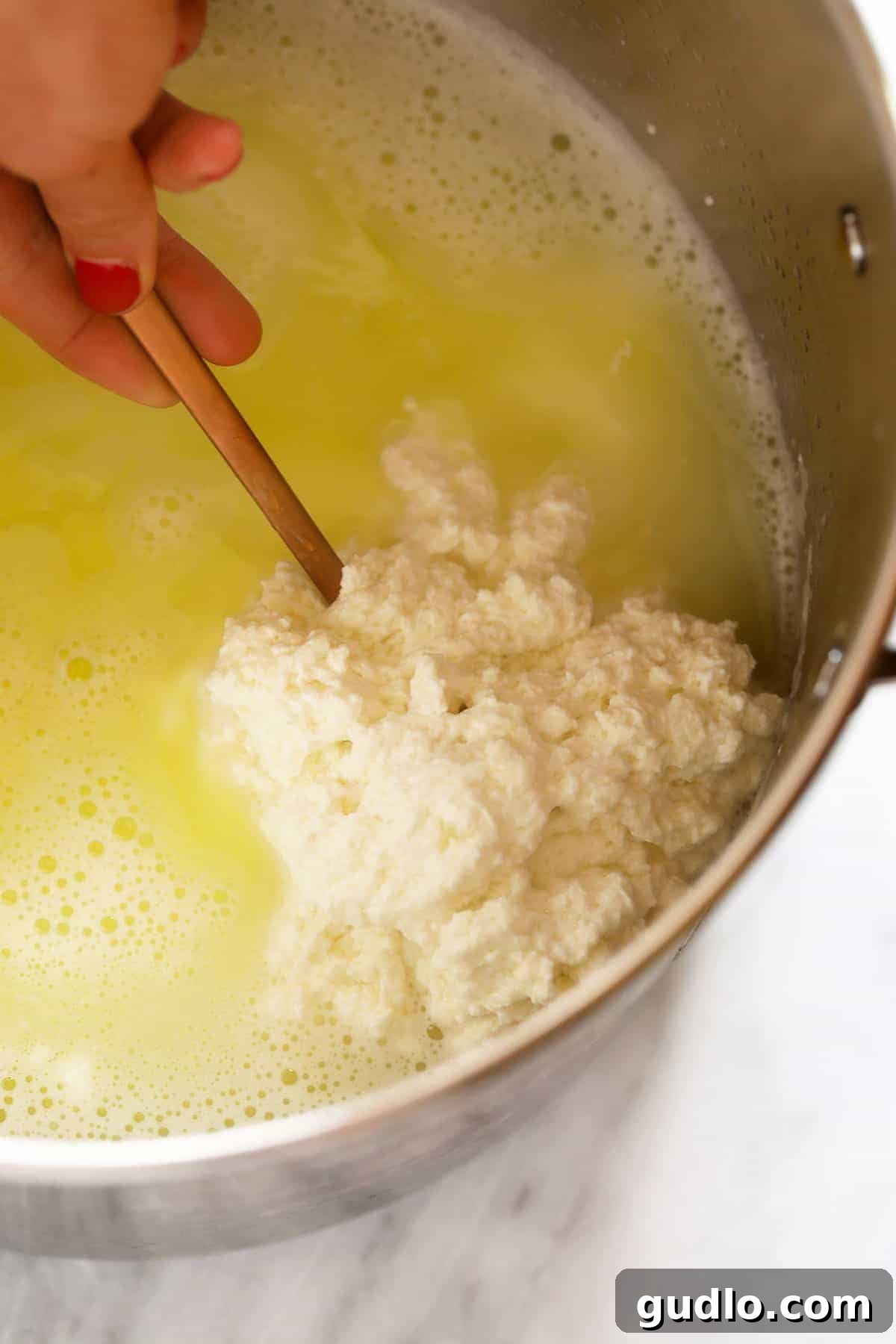 Crafting Fresh Paneer at Home 4 Fluffy white paneer curds separated from greenish-yellow whey in a stainless steel pot, indicating successful coagulation.