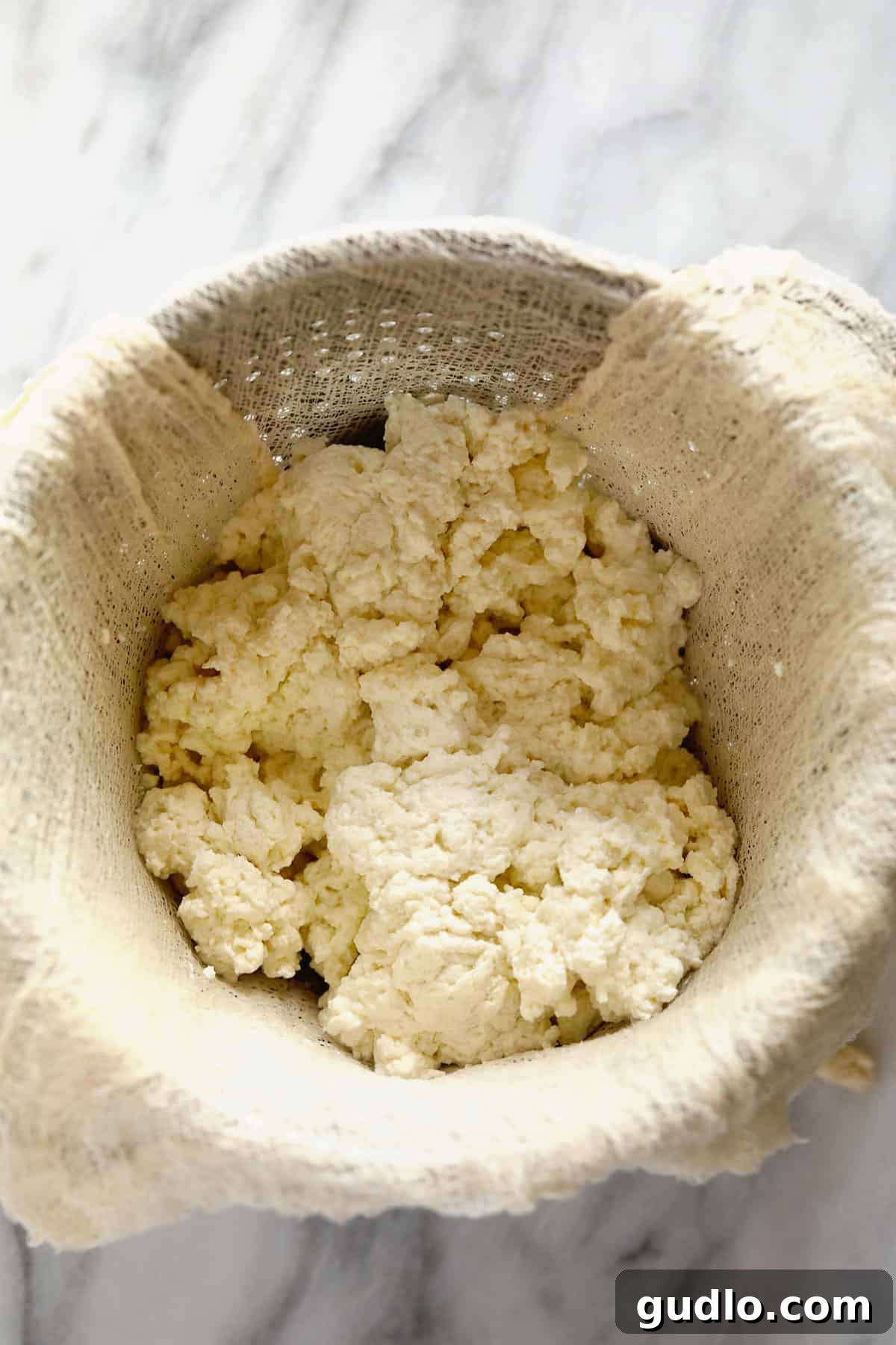 Crafting Fresh Paneer at Home 5 Soft white paneer curds gathered in a cheesecloth-lined colander, with whey draining away.
