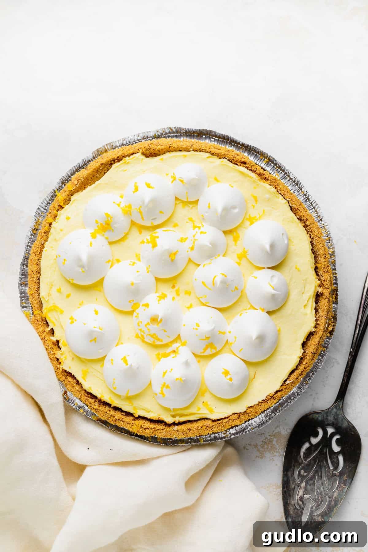 A delectable cream cheese lemonade pie beautifully adorned with a generous topping of whipped cream and delicate curls of fresh lemon zest.