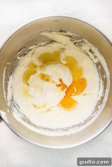 A bowl containing cream cheese, lemonade concentrate, and vanilla extract being mixed until smooth.