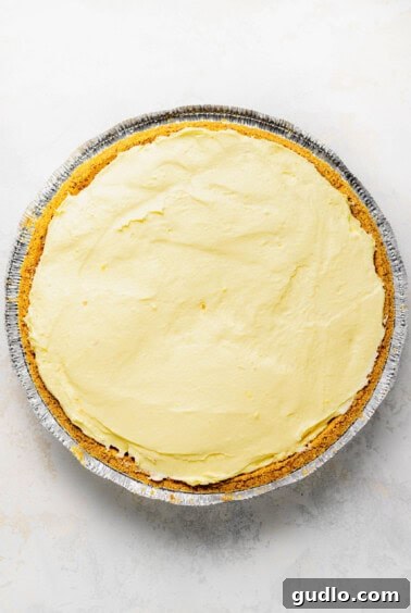 A no-bake lemon pie filling neatly spread into a graham cracker crust, ready for chilling.