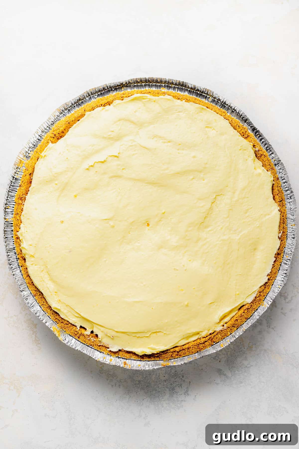 An unbaked cream cheese lemonade pie filling poured into a golden graham cracker crust, ready for chilling.